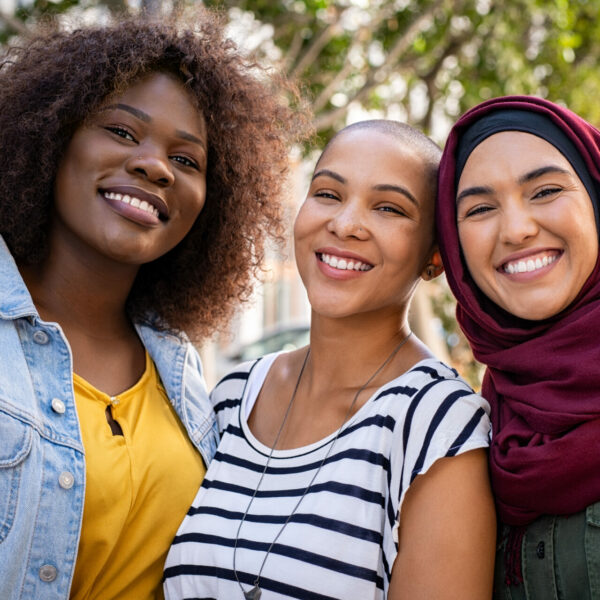 Group of three happy multiethnic friends looking at camera. Portrait of young women of different cultures enjoying vacation together. Smiling islamic girl with two african american friends outdoor.