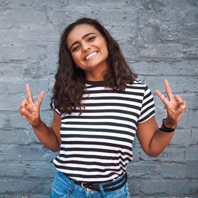 Portrait of a young woman showing the peace sign against a grey wall